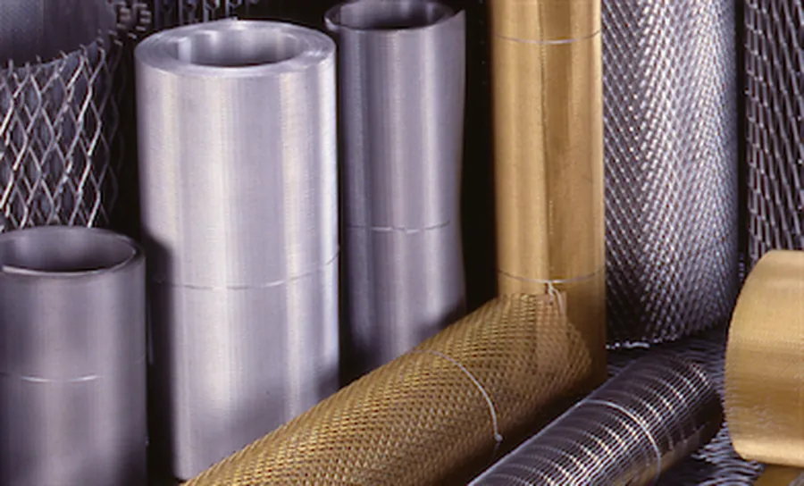 Rollos de malla de metal desplegado AHOSA en distintos metales: fierro, galvanizado, aluminio, cobre y bronce, apilados en bodega.